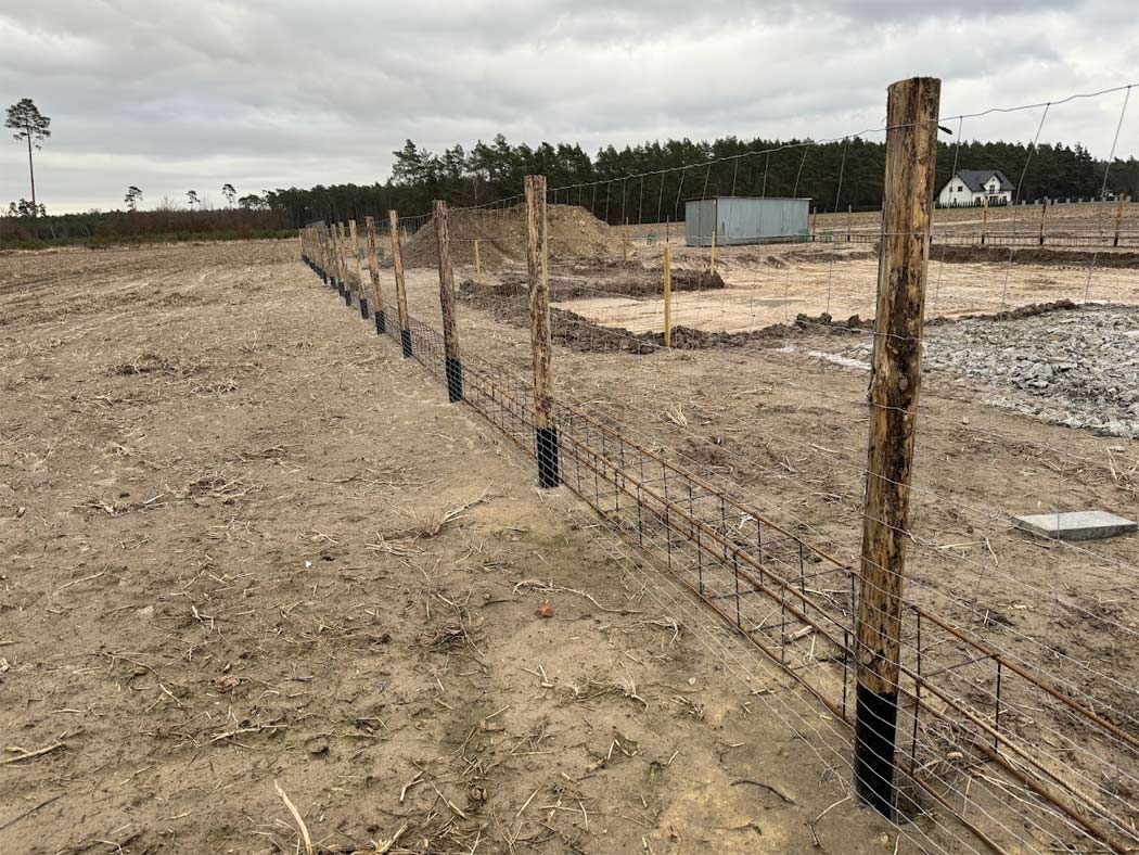 Ogrodzenie budowy wykonane z siatki leśnej na słupkach drewnianych